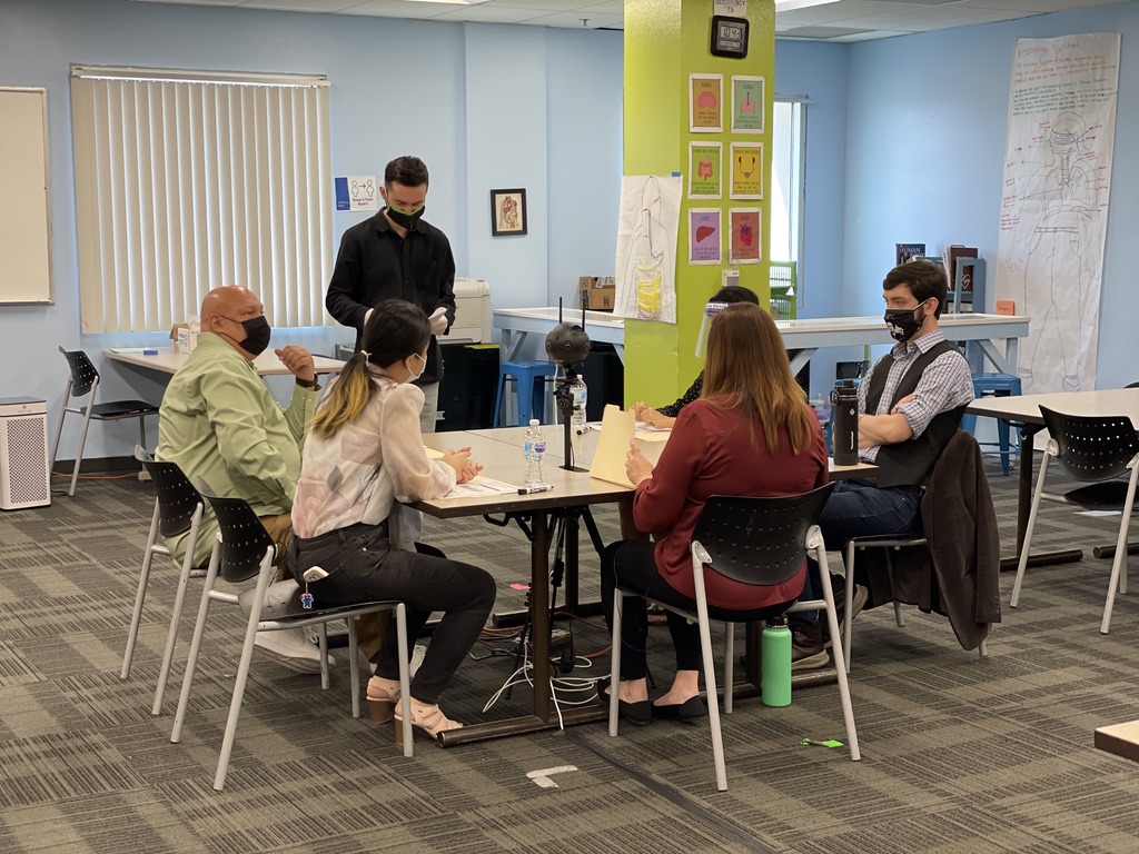 Actors with Director Ethan Garcia between takes of filming a teacher meeting scenario